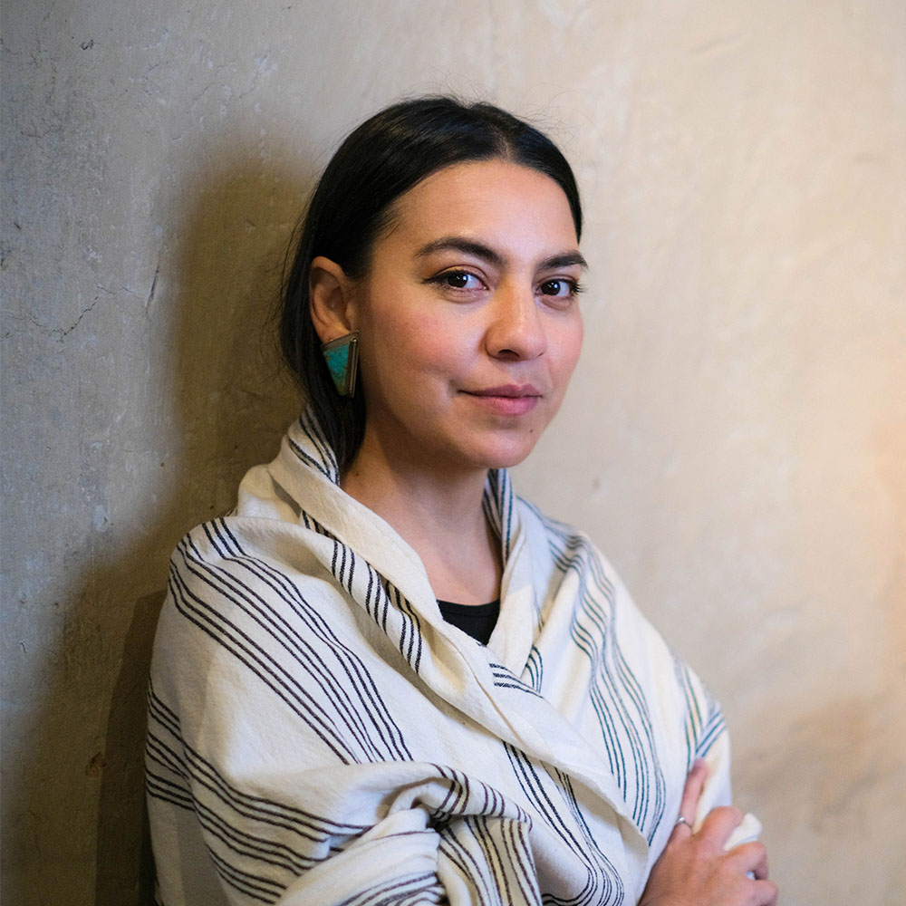  A young woman with black hair against a textured wall.